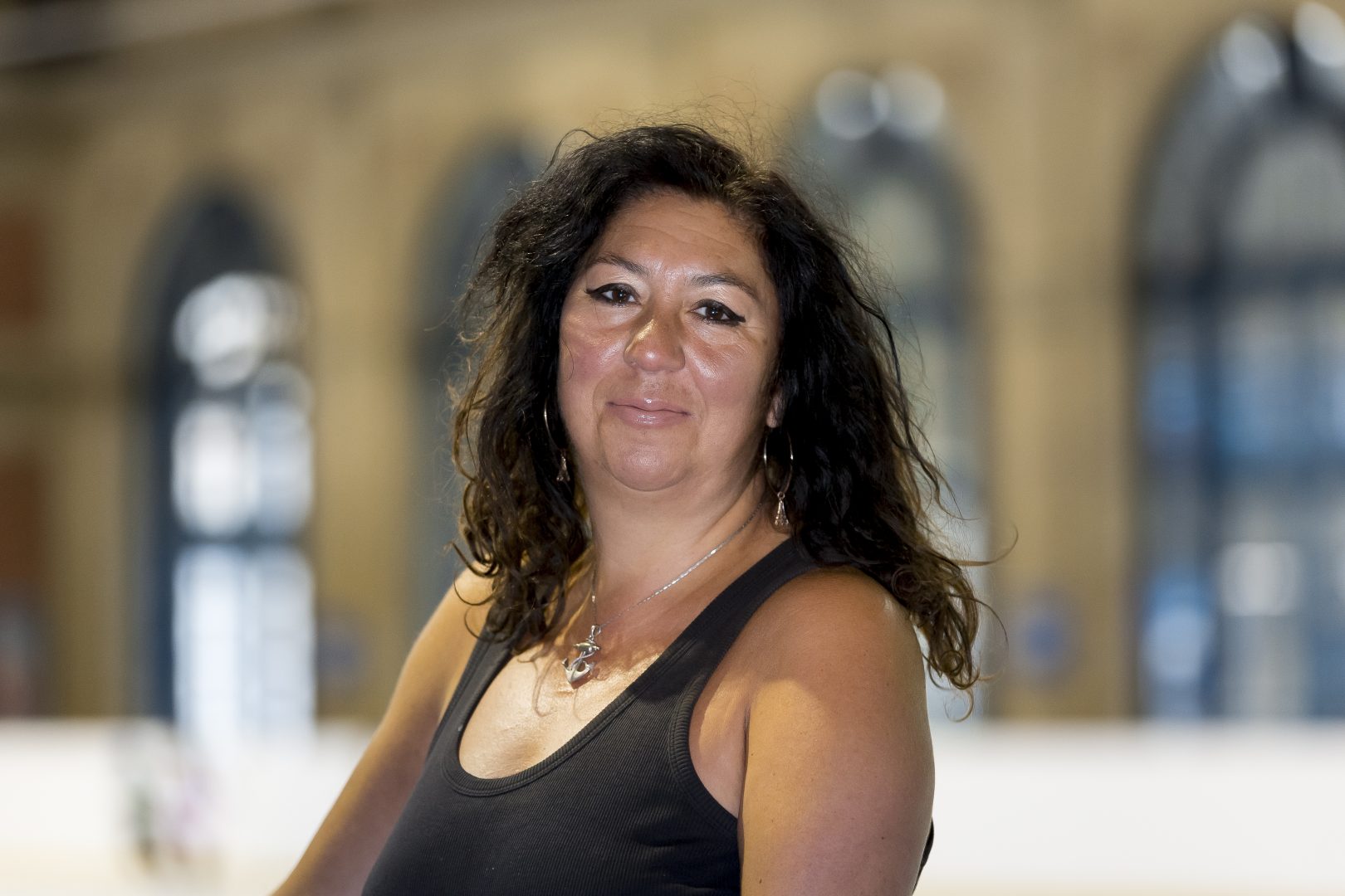 Woman with dark hair and a black vest standing on an ice rink smiling