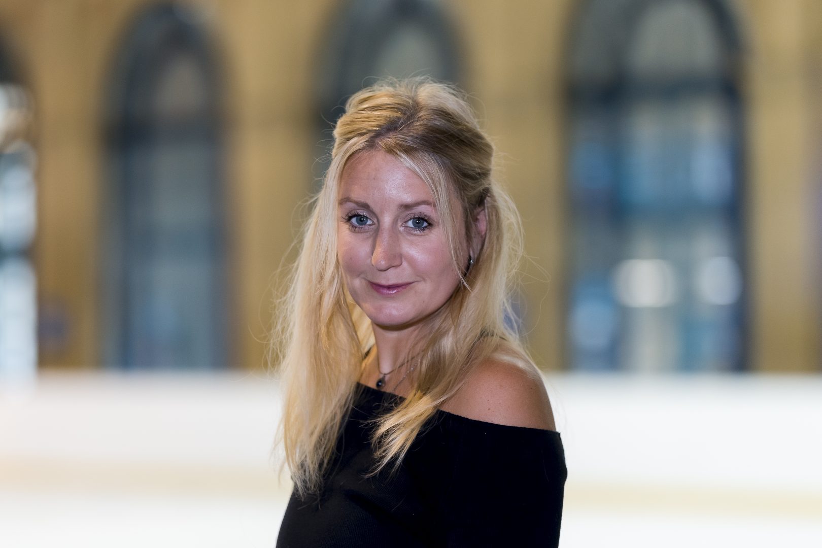 Woman with light hair and black stop smiles whilst standing on an ice rink