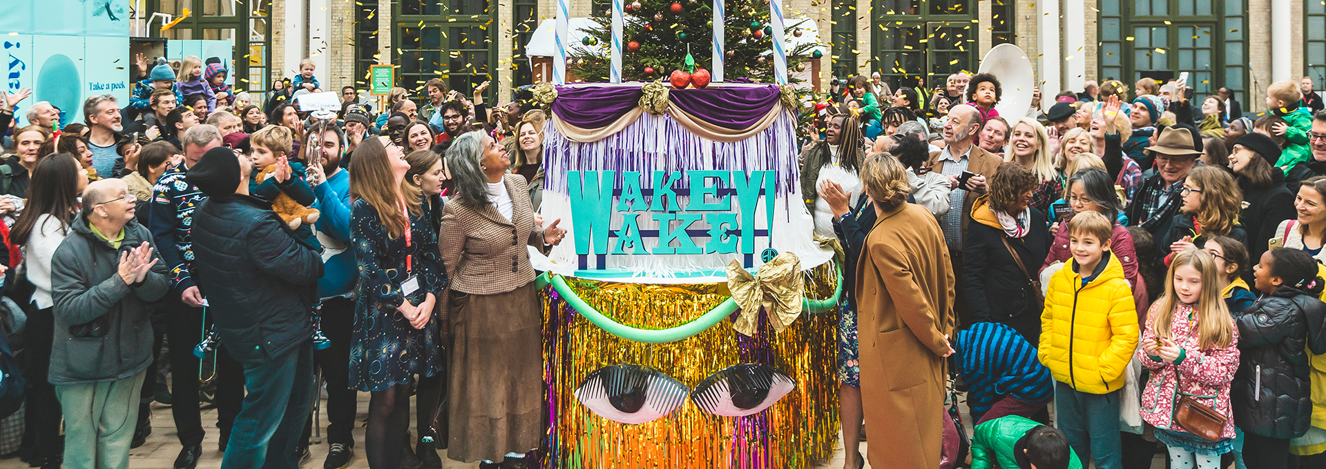 Group of people looking at a glittery stall which reads 'wakey wakey' as confetti falls.