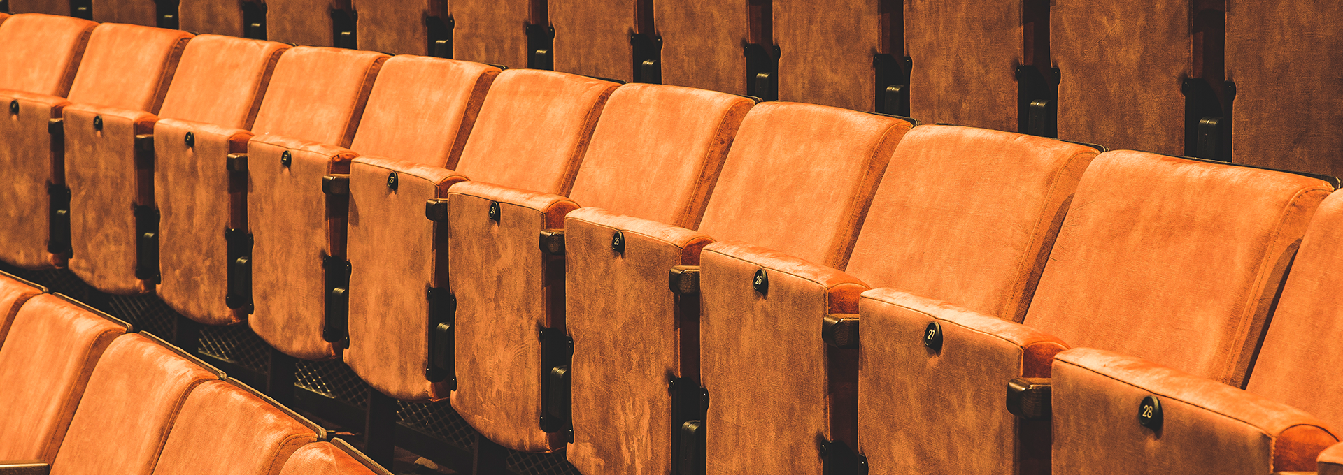 A row of empty orange theatre seats with the seats lifted up.