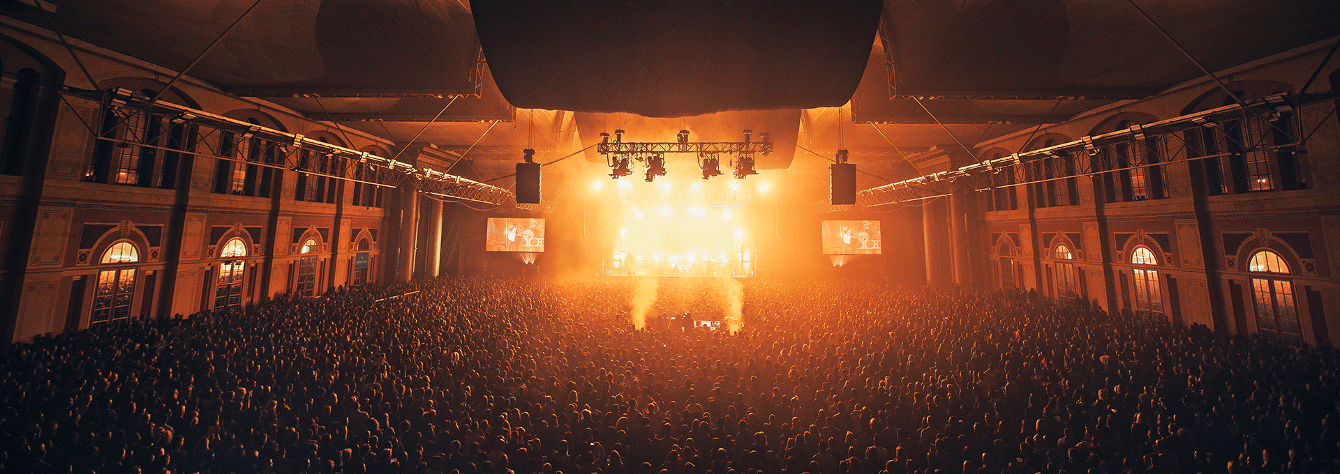 Large audience with golden light experiencing a concert in the Great Hall at Ally Pally.