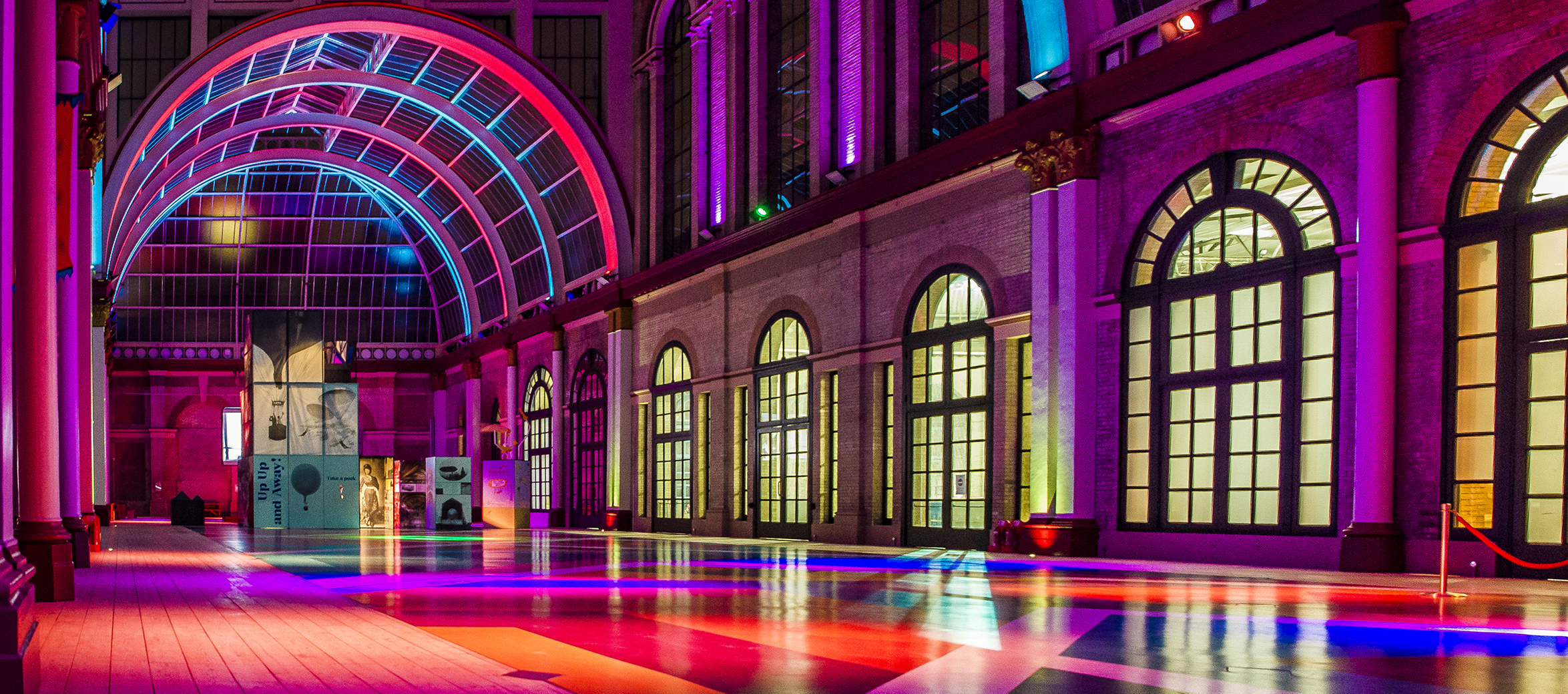 The East Court at Alexandra Palace, an open colourful space, which has been lit up in pink, purple and blue lights.