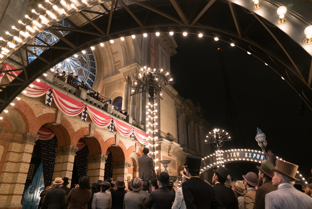 People in top hats listening to a speaker in front of Alexandra Palace as part of a filming location.